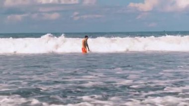 Atletik adam Endonezya 'nın Bali kıyısındaki öfkeli Hint Okyanusu' nda yüzüyor. Beyaz köpüklü büyük sörf dalgaları kameraya yaklaşıyor. Aşırı boş zaman..