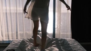 Güneşli bir günde denize bakan panaramik bir pencerenin zemininde şeffaf bornozlu bir kadın yatakta dans ediyor. Mutluluk, neşe ve tatmin duygusu. Arka plan.