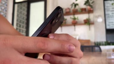 4 bin. iPhone 12 akıllı telefonu kullanan, parmaklarını bastıran, sosyal medya interneti okuyan, metin yazan ya da online alışveriş yapan bir adam. Kafede cep telefonu iki elle. 09.04.22 Bali, Endonezya.