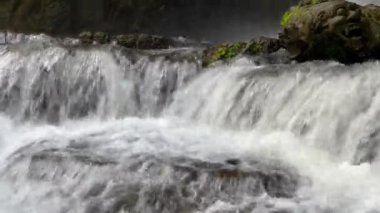 Close-up side view of cascading waterfall rapidly flowing down the rocks in the rainforest. Sumampan Waterfall in Ubud in Bali, Indonesia. 4K Video