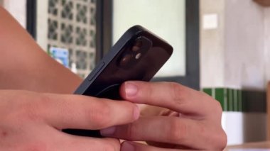 4 bin. iPhone 12 akıllı telefonu kullanan, parmaklarını bastıran, sosyal medya interneti okuyan, metin yazan ya da online alışveriş yapan bir adam. Kafede cep telefonu iki elle. 09.04.22 Bali, Endonezya.