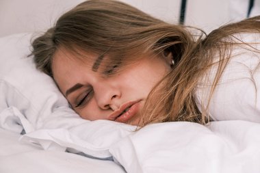Hangover. Close-up of the grimacing face of a sleeping young woman the morning after drinking alcohol. Girl feels unwell and feels uncomfortable. Headache, nausea and signs of alcohol poisoning