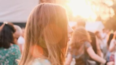 Young trendy woman listens to music and dances in rays of setting summer sun. Group of people enjoy moment at open air music festival. Energy of people, slow motion, close-up. Soft focus, 4k.