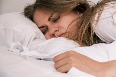 Hangover. Close-up of the grimacing face of a sleeping young woman the morning after drinking alcohol. Girl feels unwell and feels uncomfortable. Headache, nausea and signs of alcohol poisoning