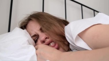 Hangover. Close-up of the grimacing face of a sleeping young woman the morning after drinking alcohol. Girl feels unwell and feels uncomfortable. Headache, nausea and signs of alcohol poisoning
