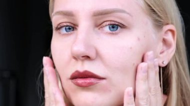 Güzel yüzlü kadınların yakın çekimi. Genç mavi gözlü sarışın kız kameraya bakarken yüzüne dokunuyor. Yüz ve vücut için yaşlanma önleyici cilt bakımı. Gençliğin uzaması ve cildin tazeliği.