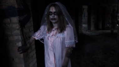 Cadılar Bayramı. Ölü gelin. Zombi makyajı ve gelinlik giymiş bir kadın terk edilmiş bir binanın karanlık koridorlarında kameraya bakarak yürüyor. Korku, ölüm ve zombi konsepti