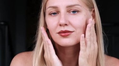 Güzel yüzlü kadınların yakın çekimi. Genç mavi gözlü sarışın kız kameraya bakarken yüzüne dokunuyor. Yüz ve vücut için yaşlanma önleyici cilt bakımı. Gençliğin uzaması ve cildin tazeliği.