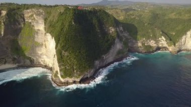 Nusa Penida island, Kelingking beach. Top view aerial shot of a sandy clean beach with clear blue and turquoise water. Rocks and waves with white foam