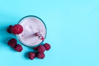Ahududulu milkshake ve açık arkaplan manzaralı kırmızı dekor. Dondurma, süt ve böğürtlen kokteyli kopi uzayının mavi arka planında