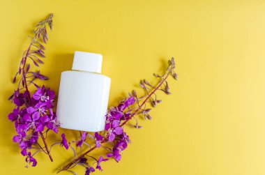 Renkli arka planda leylak renkli kır çiçekleri ve beyaz bir şişe kozmetik. Hafif bir arkaplanda çiçekler ve kozmetik metin için bir yer