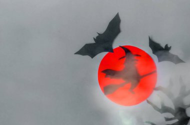 Bir kara cadı sisli bir süpürgede ve yarasalar kırmızı ayın arka planında uzay mayınının gri arka planında.