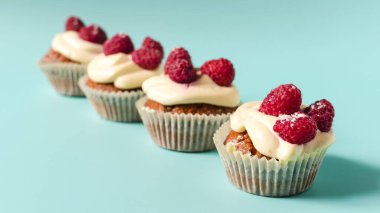 Beyaz kremalı ve ahududulu kekler ön planda mavi arka plan keskinliği üzerine dizilmişler. Renkli arka planda ev yapımı tatlı kekler..