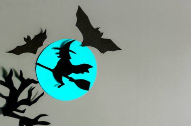 Mavi ayın arka planında yarasalarla çevrili bir süpürge üzerinde uçan siyah bir cadının gölgesi..