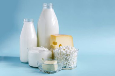Süt ürünleri yakın planda. Mavi arka planda şeffaf tabaklarda. Süt, kefir, ekşi krema, peynir, tereyağı ve süzme peynir açık arkaplanda cam bir kapta.