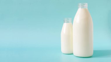 Mavi arka planda iki bardak süt. Renkli bir arka planda cam şişelerde bir litre süt ve 0.5 litre süt. Mesaj için bir yer.