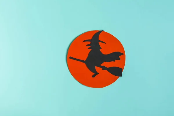 Shadow of a black witch in a hat on a broom against the background of a red moon close-up. Colorful minimalist picture for Halloween