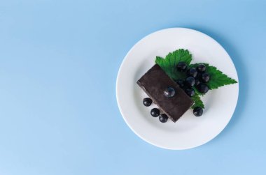 Kahverengi kremalı kek, siyah frenk üzümü yaprakları ve beyaz tabakta böğürtlen. Siyah böğürtlen ve kek renkli bir arkaplan kopyalama alanı