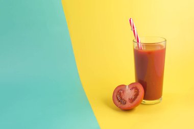 Şeffaf bir kâse içinde taze domates suyu ve yarım domates. Mesaj için sarı-yeşil arka planda.