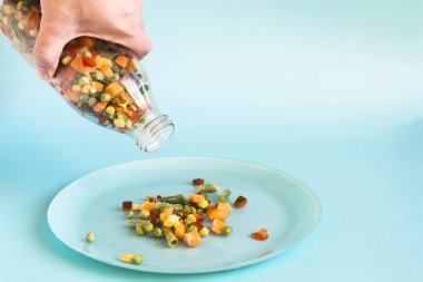 The concept of using quick-frozen foods, a hand holding a bottle with a mixture of frozen vegetables