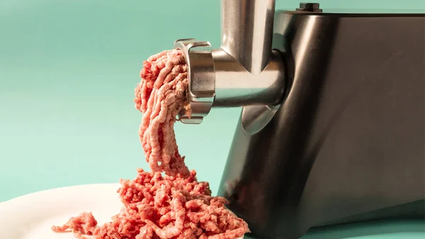 Electric meat grinder for households processes meat on a light banner background.