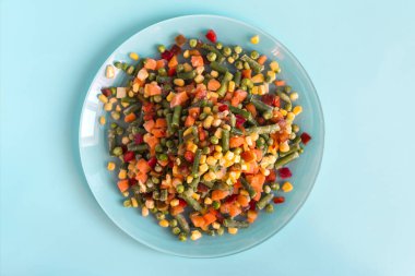 Hızlı dondurulmuş ürünler kullanma kavramı. Donmuş sebzeler açık bir tabakta, parlak mavi arka plan görünümünde..