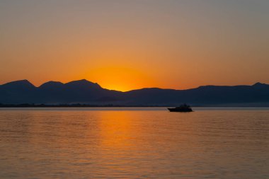 Dağ ve tekneyle ufukta gün doğumu. Finike, Antalya, Türkiye