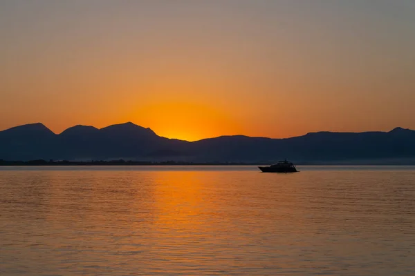 Sunrise on the horizon with mountain and boat. Finike, Antalya, Turkey