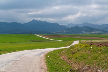 Dolambaçlı bir köy yolu ve arka planda dağlar..