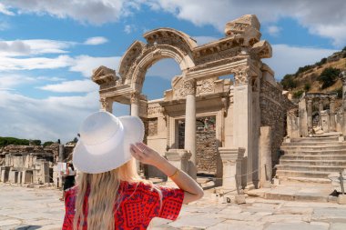 Türkiye 'nin Efes kentinde, Efes, İzmir, Türkiye' nin güneşli bir yaz gününde, kırmızı elbiseli ve beyaz şapkalı bir kız, antik Efes kentinde Hadrian Harabeleri Tapınağı 'nı izliyor