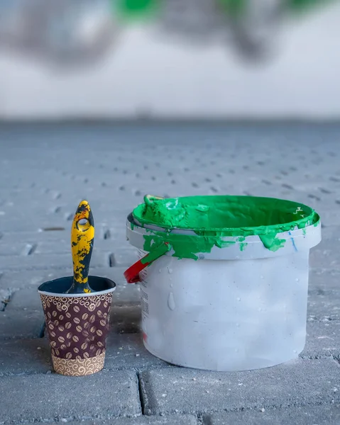 Green paint in a bucket and blurred  murals arts working in the background