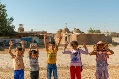 Sanli Urfa, Türkiye - 12 Eylül 2020: Harran sokaklarında eşsiz Harran evlerinin önünde el kaldıran çocuklar.