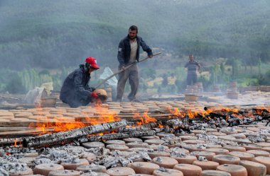 Mihaliccik, Eskisehir / Türkiye-26 Temmuz 2020: Kadın işçiler açık havada yanan ahşap aracılığıyla kil çömlek kurutuyorlar.