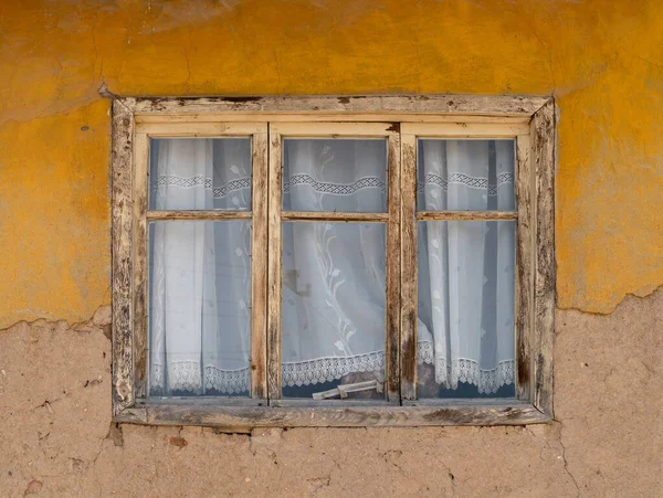 Wooden window of a house with old adobe walls. A wooden window with a white curtain. Exterior view.