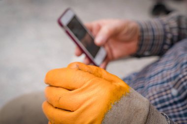 Sarı eldiven giyen işçi tatilde cep telefonuna bakıyor.