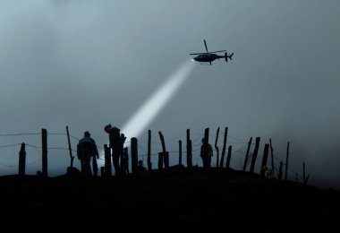 Dikenli tellerin diğer tarafındaki göçmenlerin silueti ve helikopter onları havaya kaldırıyor..