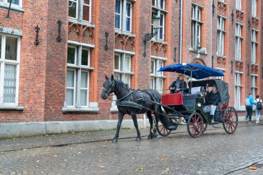 Bruges, Belçika - 11 Ekim 2019: At arabası sokakta ve turist şoförün fotoğrafını çekiyor.