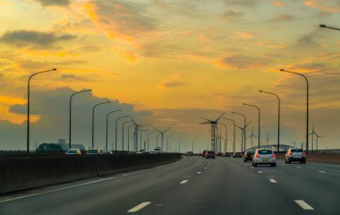 Anvers / Belçika - Ekim 05: 2019: Altın gökyüzü parlıyor ve araba rüzgar enerjisi tribünüyle altın gökyüzüne doğru koşuyor.