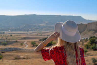 Beyaz şapkalı genç bir kadın yolu izliyor ve birini bekliyor. Bir kadın gelişini bekliyor. Dağ ve vadiyi, Kapadokya, Türkiye