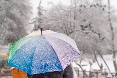 Parkta kar altında gökkuşağı şemsiyesi kullanmak