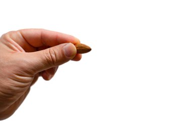 İzole edilmiş beyaz arkaplanı olan bir badem çekirdeğini tutan insan parmağı