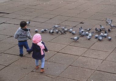 Kimliği belirsiz bir çocukla kızın güvercinleri besleyip günün tadını çıkardıkları arka plan.