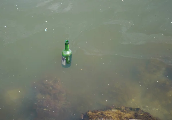 緑のガラス瓶は汚れた水に浮かび 環境を汚染します — ストック写真