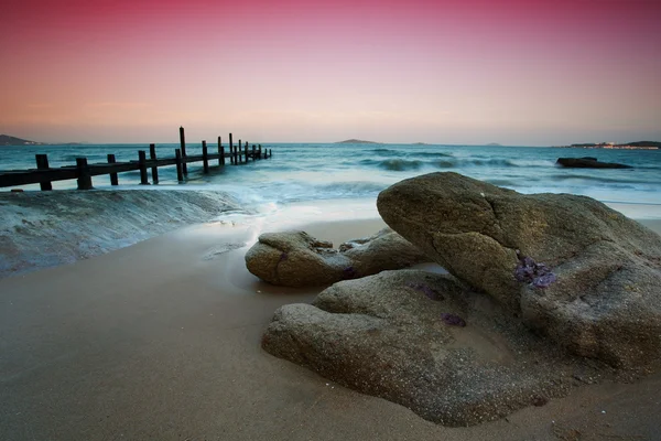 Rocks on the beach and wooden pier — Stock Photo, Image