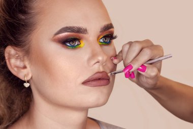 Professional makeup artist applies lip contouring on beautiful model lips creating glamour make-up