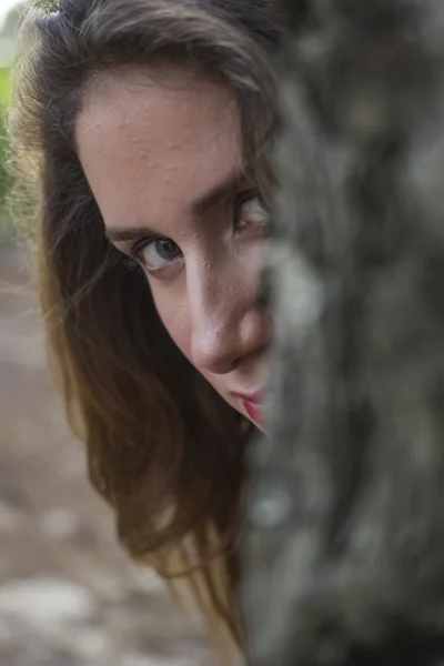Ung tjej söker bakom ett träd — Stockfoto