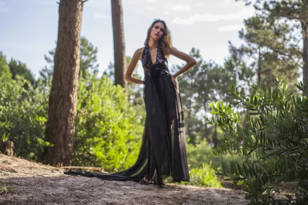 Linda joven modelo en vestido negro solo en el bosque — Foto de Stock