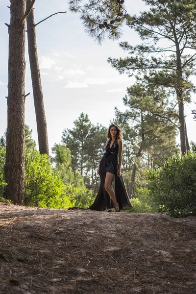 Modelo atractivo en vestido de noche negro solo en el bosque — Foto de Stock