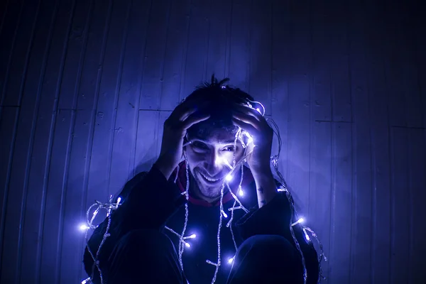 Hombre sonriendo atrapado en las luces de Navidad — Foto de Stock