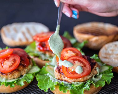 Kız ev yapımı burgerlere kaşıkla sos koyuyor. Evde lezzetli fast food hazırlıyorum, yakın plan. İşlem
